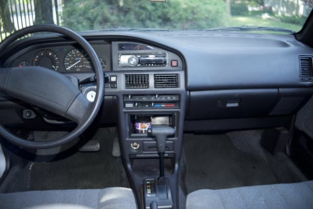 The interior center console of a 1989 Toyota Corolla showing a radio, two air vents, climate control, and ash tray.