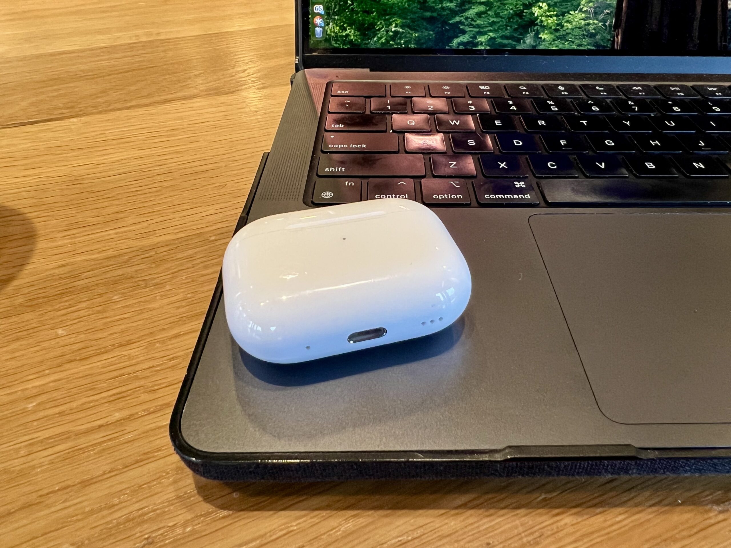 AirPods Pro case sitting on the keyboard of a black MacBook Pro to the left of the trackpad.
