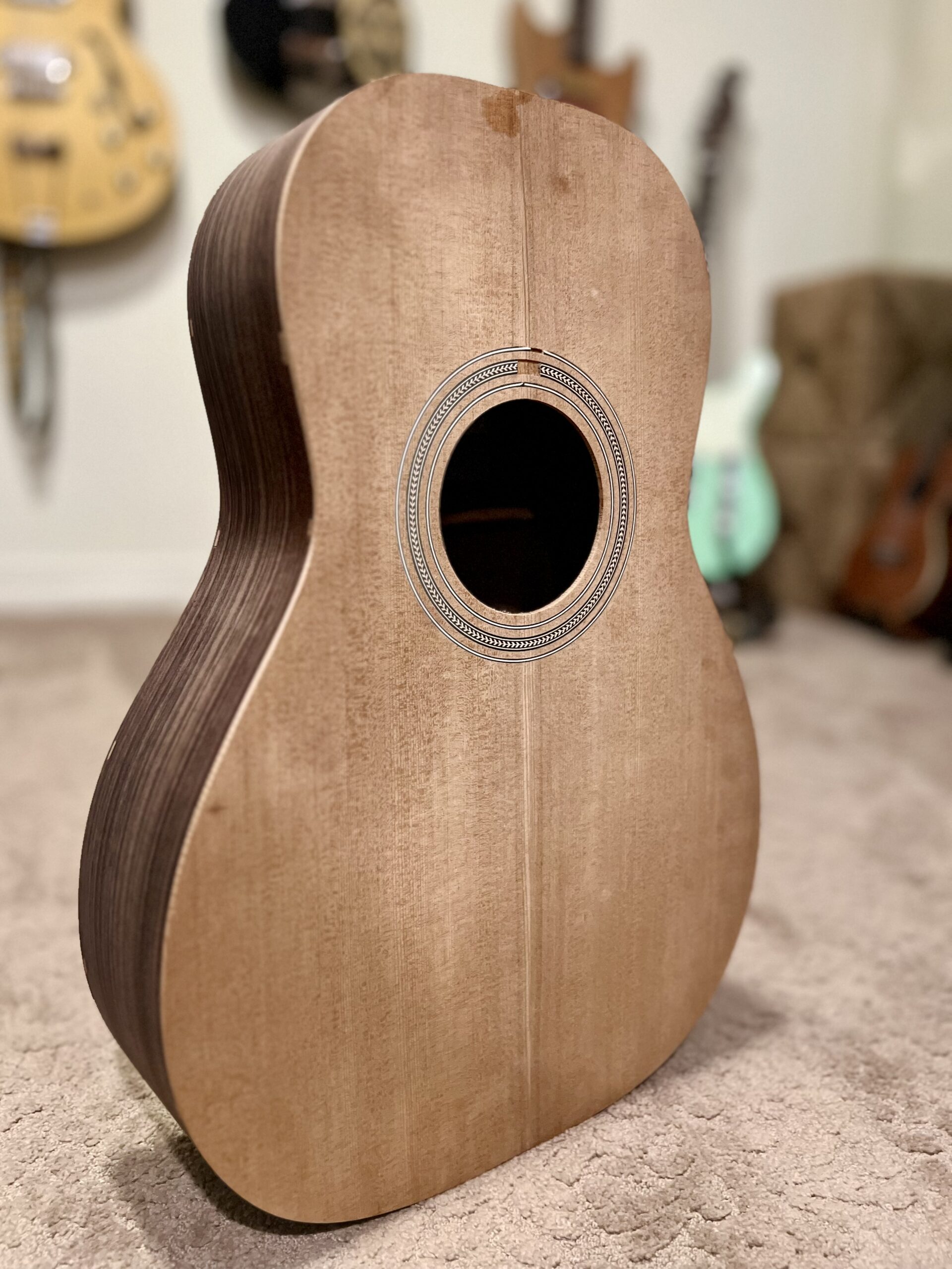 The body of a wooden acoustic guitar standing upright. The shape is there, but it needs more sanding!