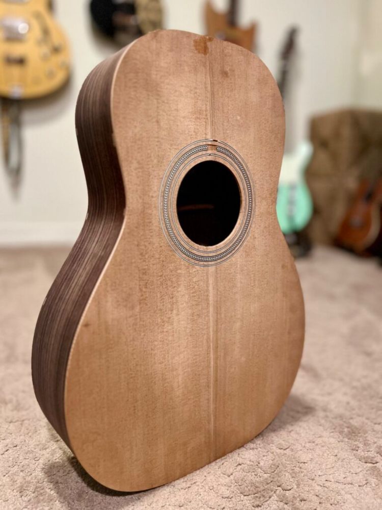The body of a wooden acoustic guitar standing upright. The shape is there, but it needs more sanding!